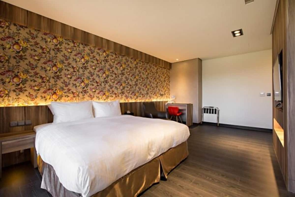 Una habitación de hotel moderna con una cama grande, un cabecero de madera, un papel tapiz con estampado floral y un escritorio pequeño con una silla.