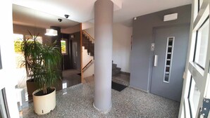 Un pasillo con un pilar grande, una planta en maceta, una escalera y una puerta con ventana.