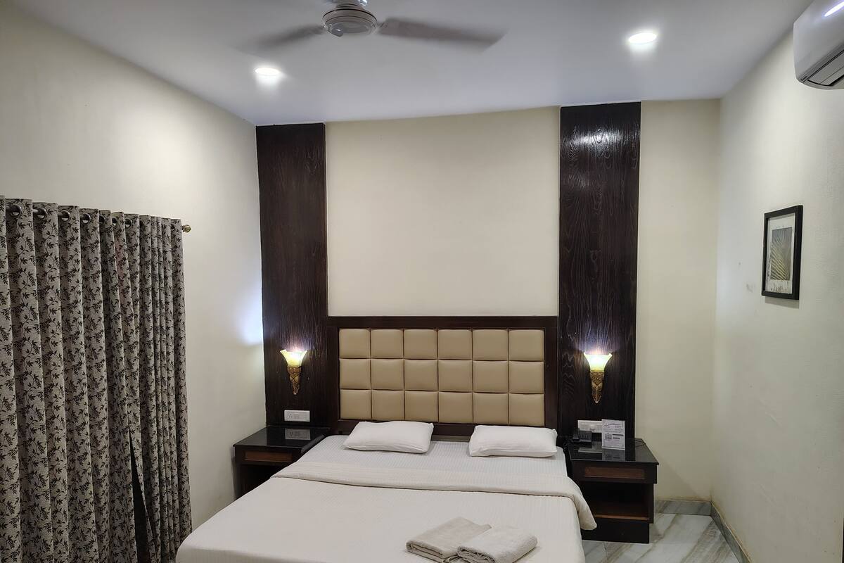 A hotel room with a bed, two bedside tables, a ceiling fan, and a window with curtains.