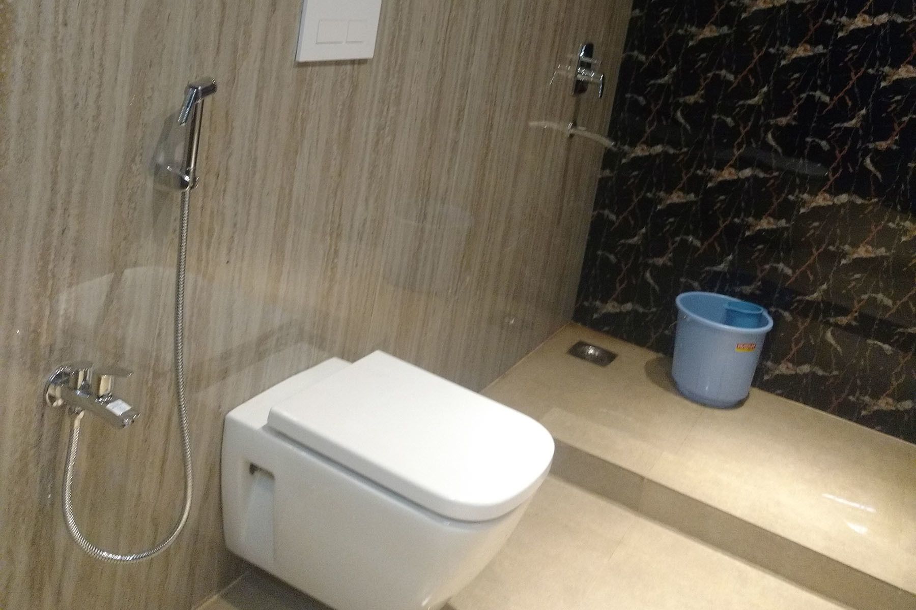 A bathroom with a toilet, a shower, and a blue trash bin.