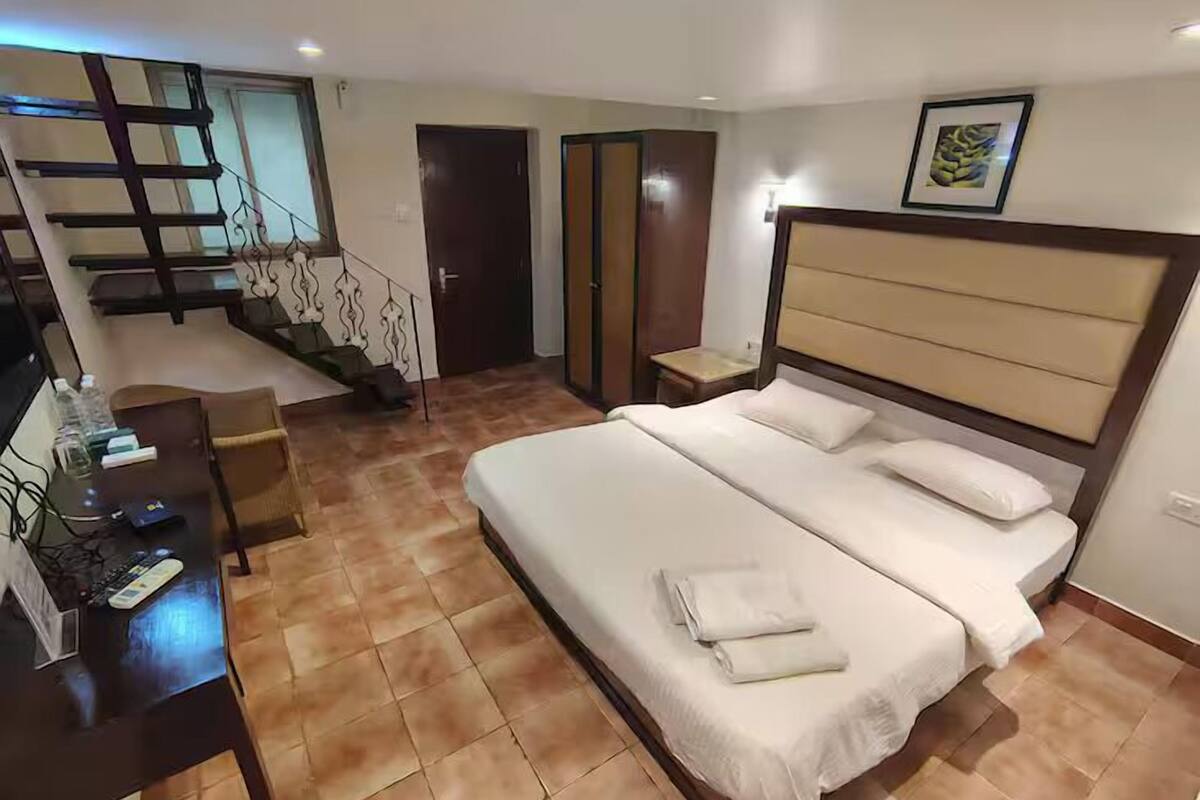 A bedroom with a large bed, a desk with a computer, and a staircase.