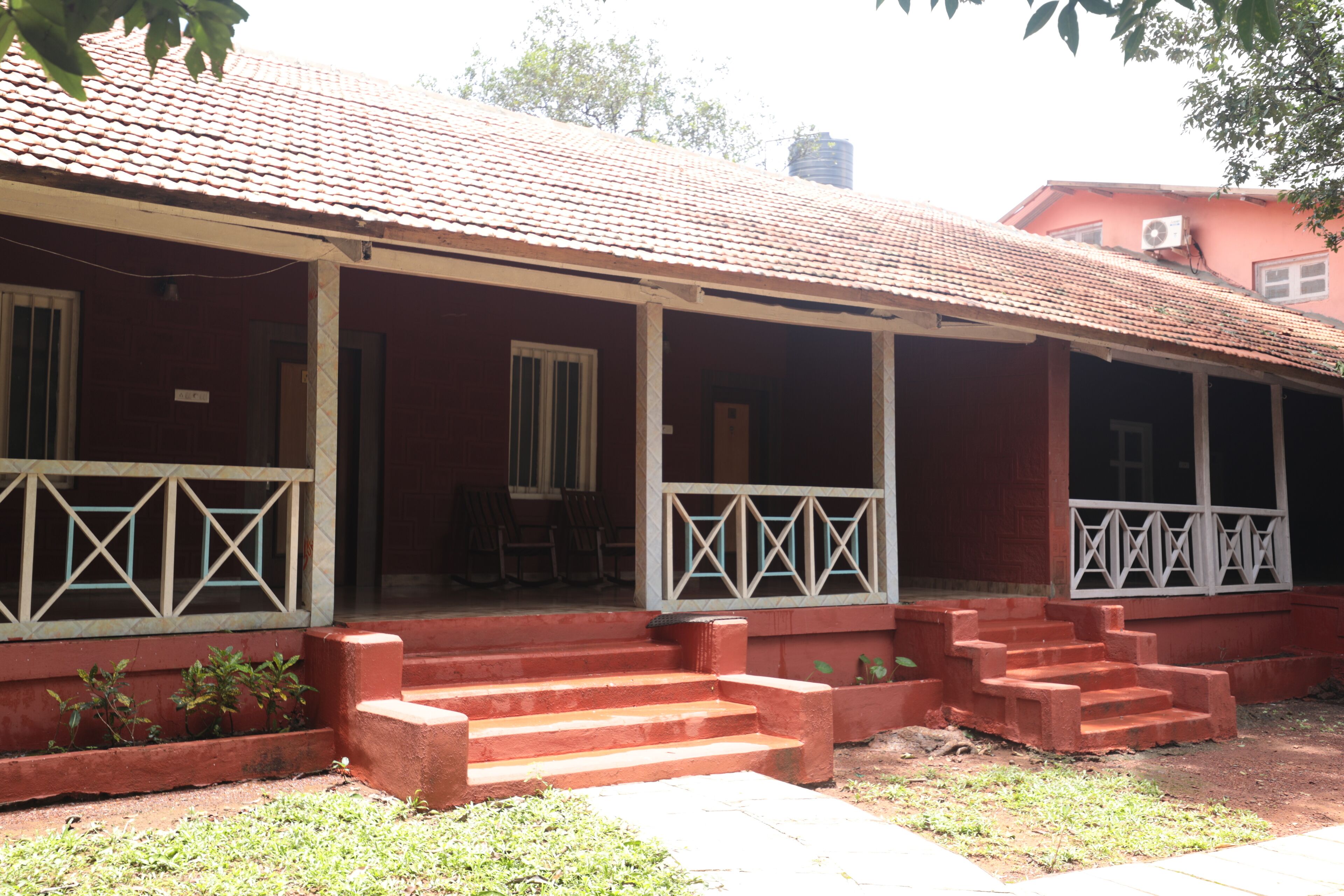 Um edifício com fachada vermelha, várias janelas com molduras brancas e um alpendre coberto com degraus que levam à entrada.