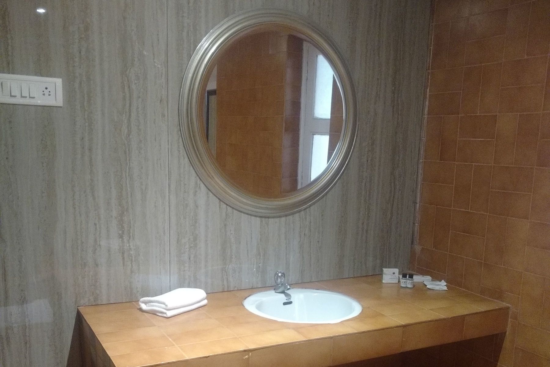 A bathroom with a round mirror, a sink, and a towel on the counter.