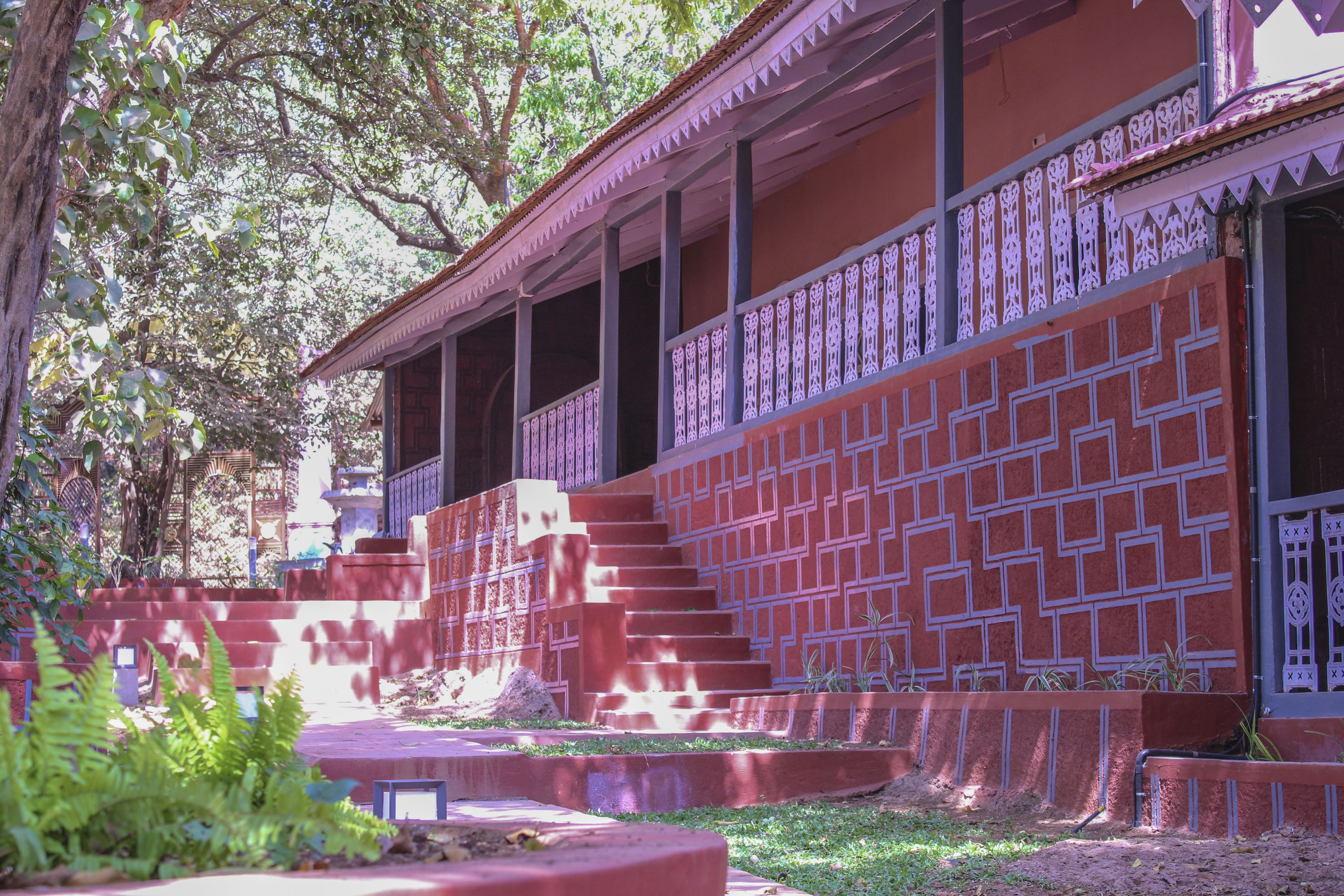 Un immeuble à la façade en briques rouges, doté d’un balcon orné de balustrades blanches finement travaillées, et d’un escalier menant à l’entrée.