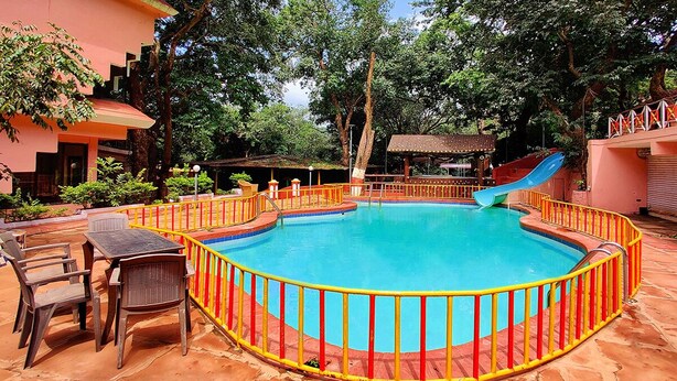 Une piscine avec un toboggan, entourée d’une clôture jaune et rouge, et dotée d’un espace extérieur pour s’asseoir.