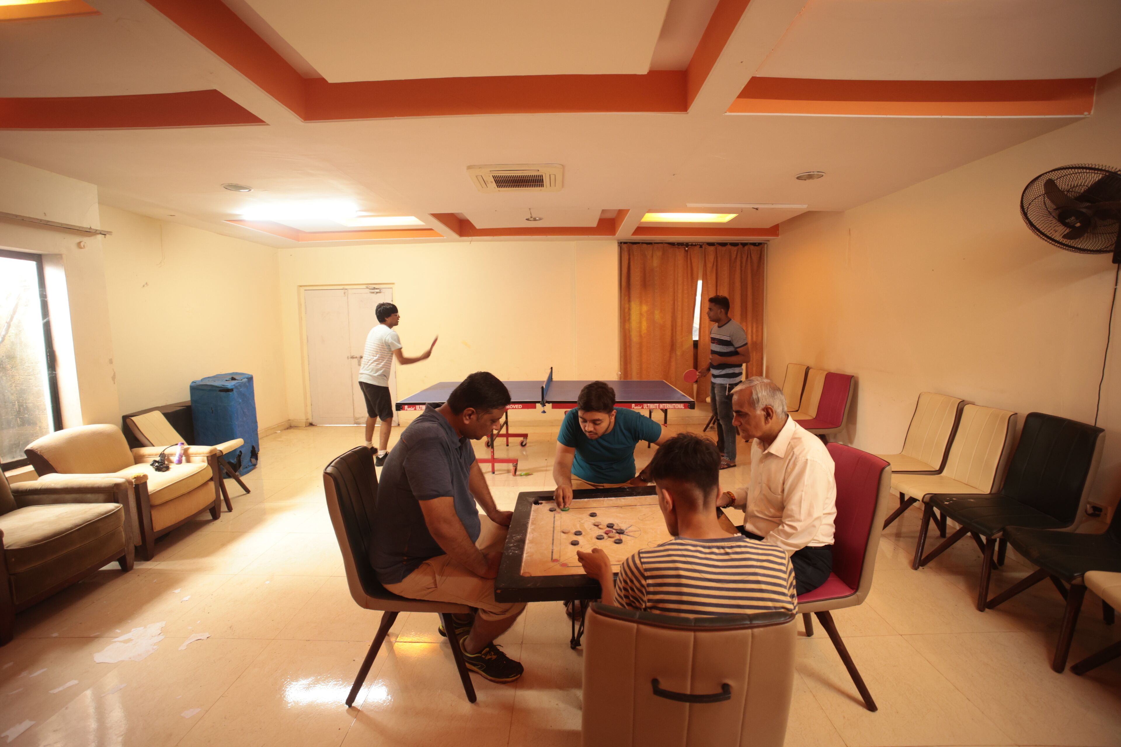 A room with a ping pong table, chairs, and a fan.