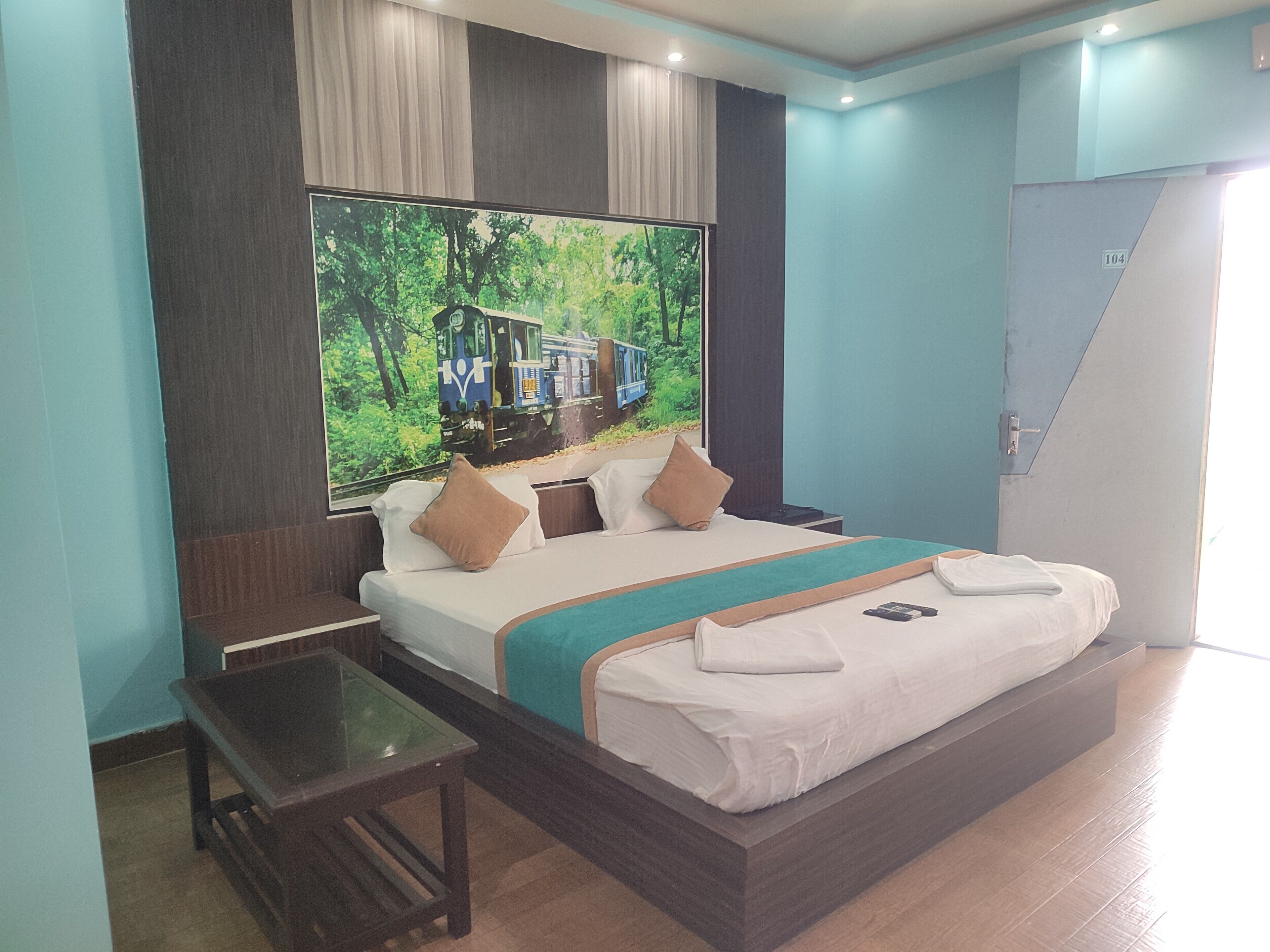 A modern hotel room with a large bed, a glass table, and a large poster of a train on the wall.