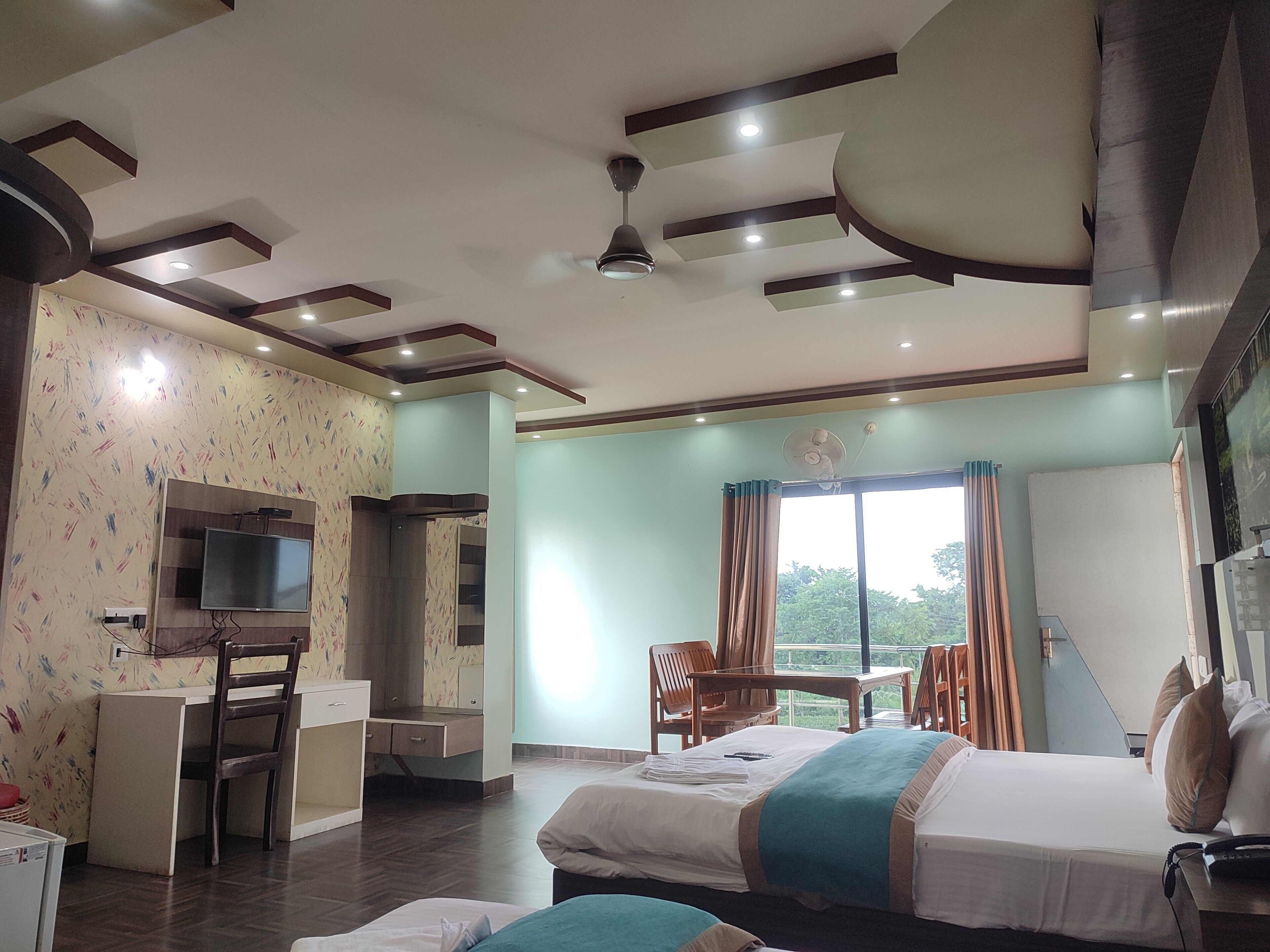 Quarto de hotel com duas camas, uma escrivaninha, televisão e varanda com vista.