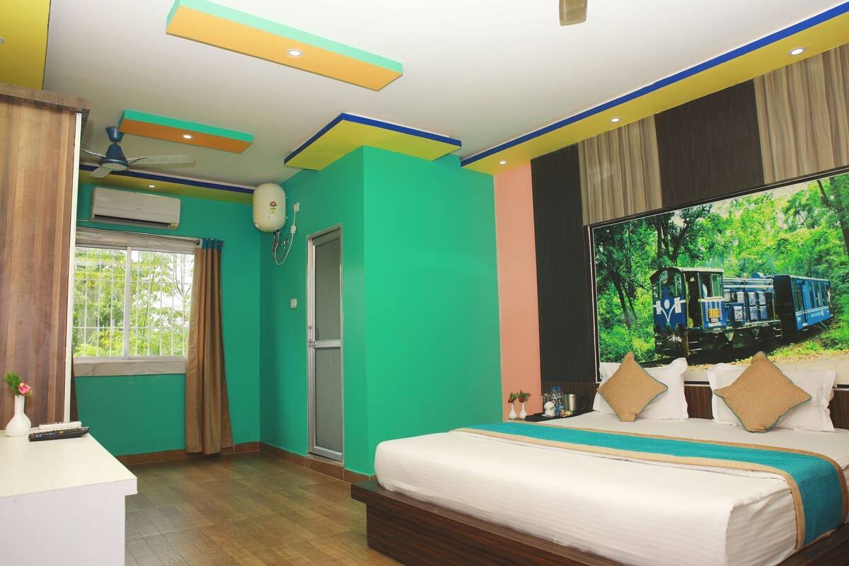 Quarto com cama, janela com vista para um trem, ventilador de teto e ar-condicionado fixado na parede.