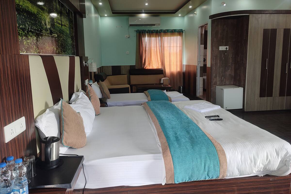Quarto de hotel com uma cama grande, uma escrivaninha com cafeteira, mini-geladeira e vista para um jardim pela janela.