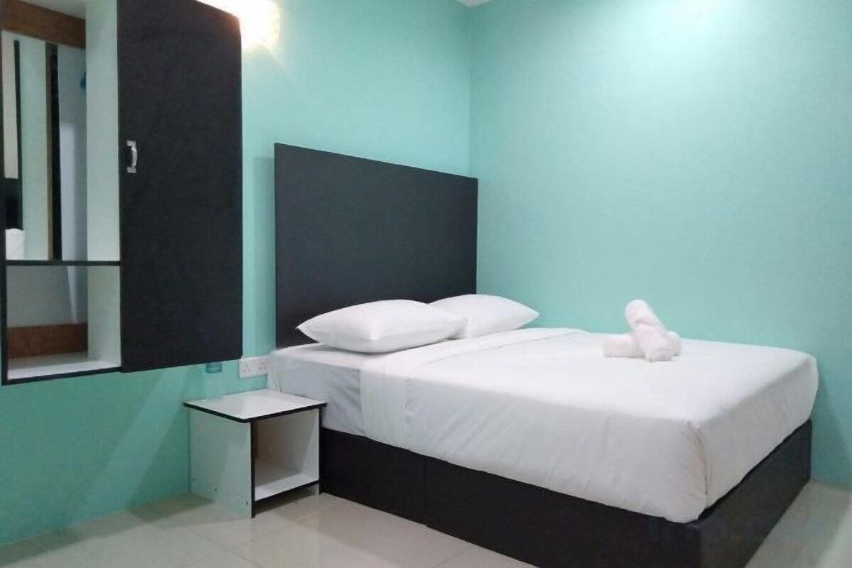 Un lit simple avec une literie blanche, une table de chevet et un miroir au mur.