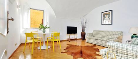 Un salón amplio con piso de madera, un tapete de cuero marrón, un sofá a cuadros, un comedor amarillo y un televisor de pantalla plana.