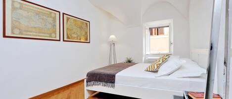 A bedroom with a bed, a lamp, and two framed maps on the wall.