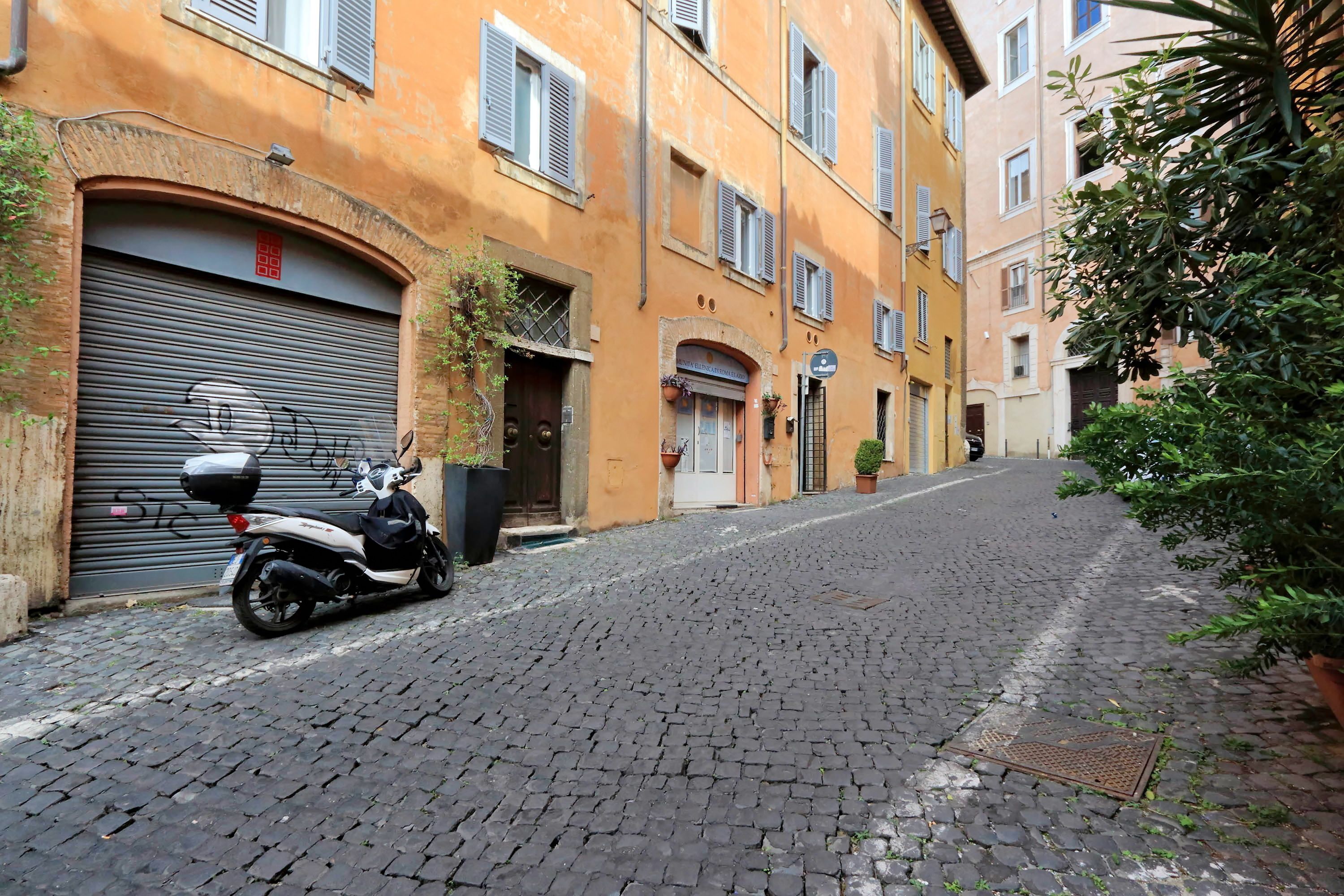 A narrow cobblestone street with a parked scooter and closed shop shutters.