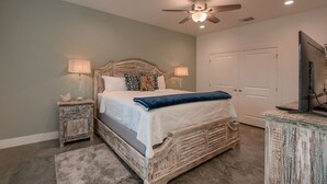 A bedroom with a wooden bed, two bedside tables with lamps, a ceiling fan, and a television on a stand. - Lone Star Cabin No. 6 (Fredericksburg)