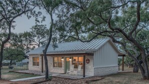 A cabin with a stone facade, a metal roof, and a porch with chairs. - Lone Star Cabin No. 6 (Fredericksburg)