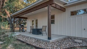 A covered patio with a table and chairs, a grill, and a stone border. - Lone Star Cabin No. 6 (Fredericksburg)