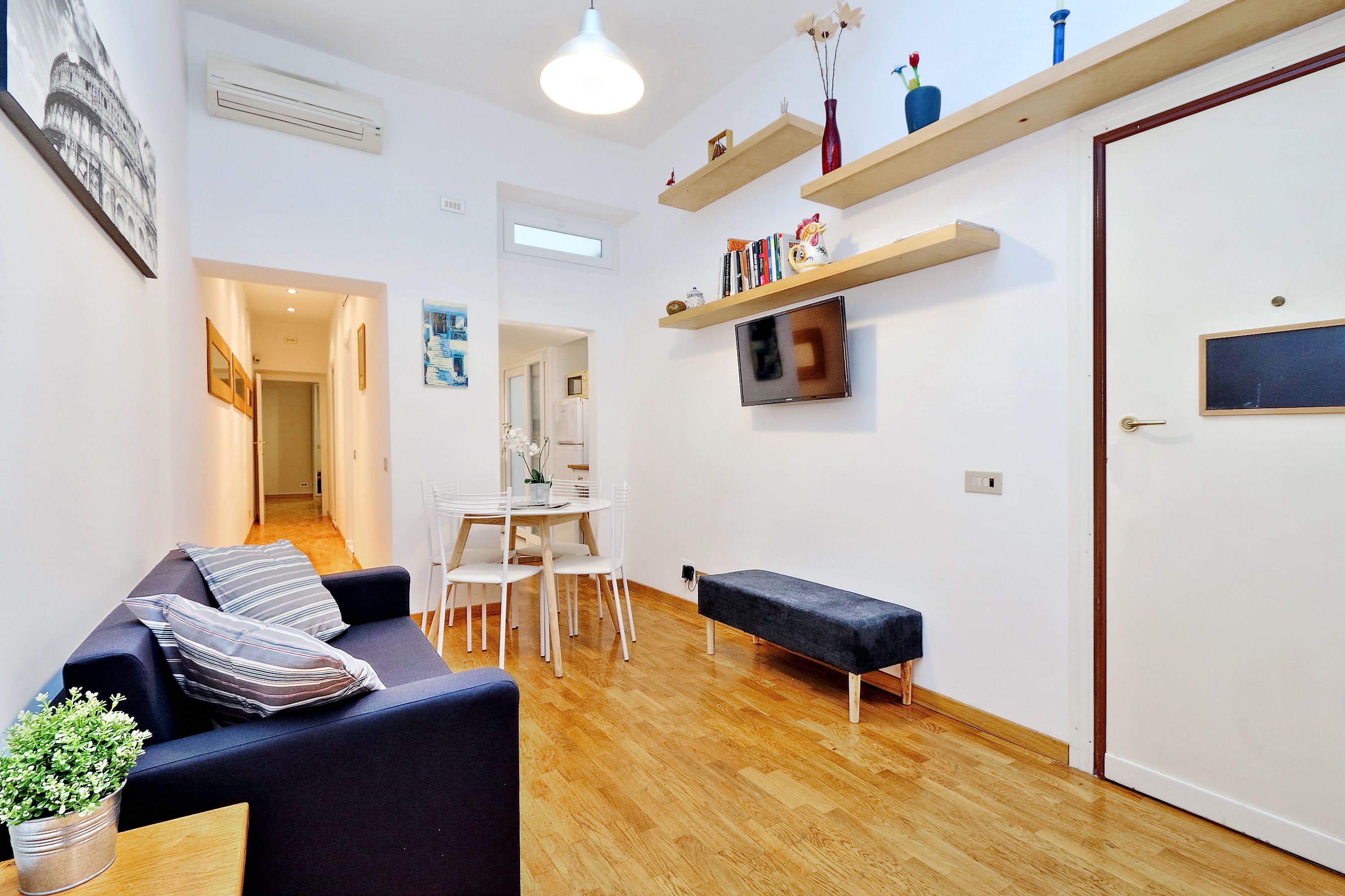 Ett modernt vardagsrum med en soffa, ett matbord med stolar, en bänk och en tv som är monterad på väggen.