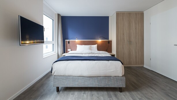 Un dormitorio moderno con una cama, un televisor montado en la pared y una ventana.