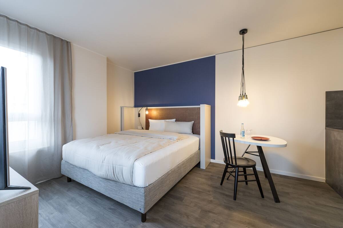 A modern hotel room with a bed, a small dining table, and a chair.
