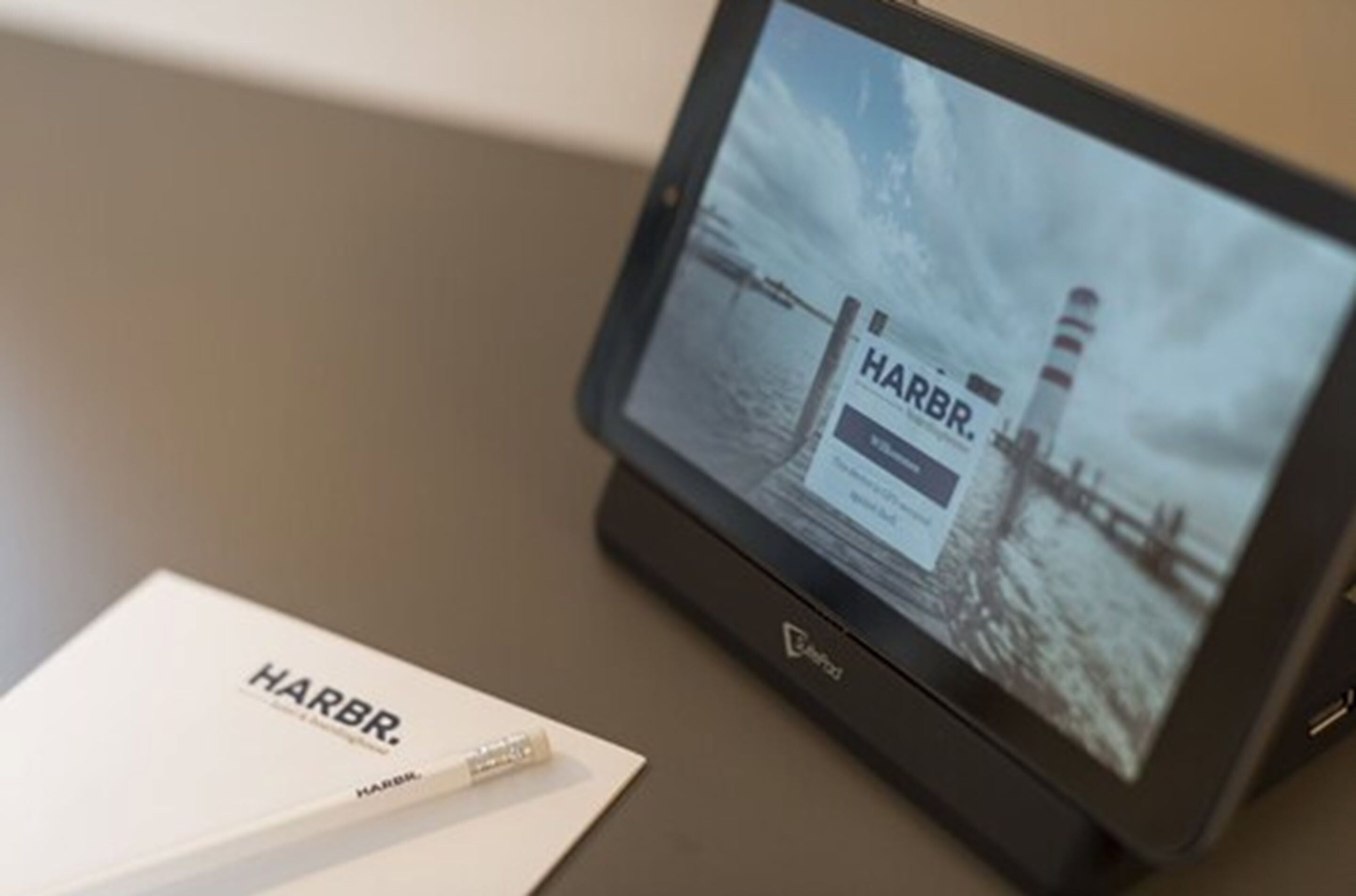A tablet displaying a Harbr logo and a coastal scene with a lighthouse.