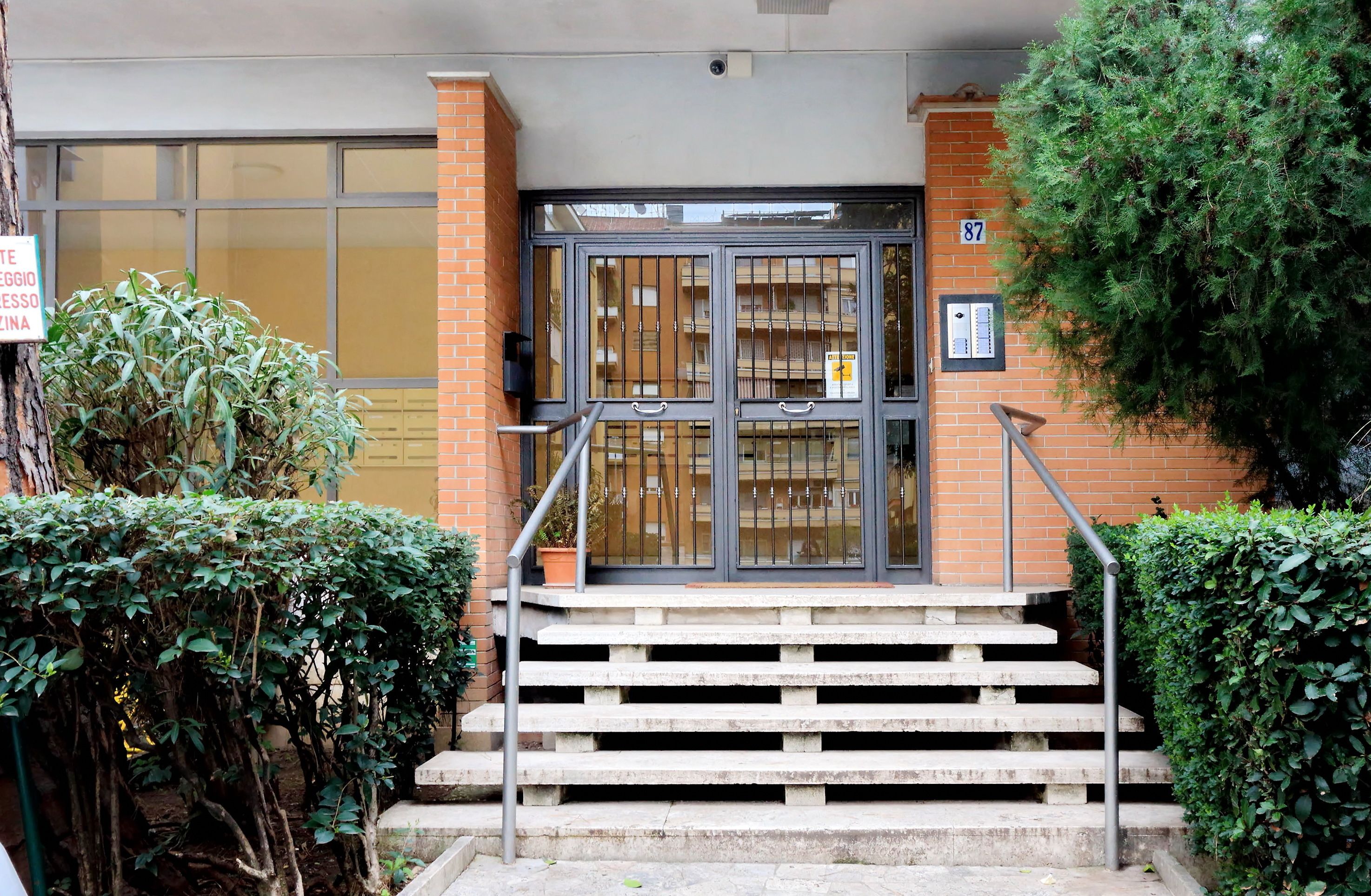 Entrada de un edificio con una verja metálica, una escalera y un cartel en la pared.