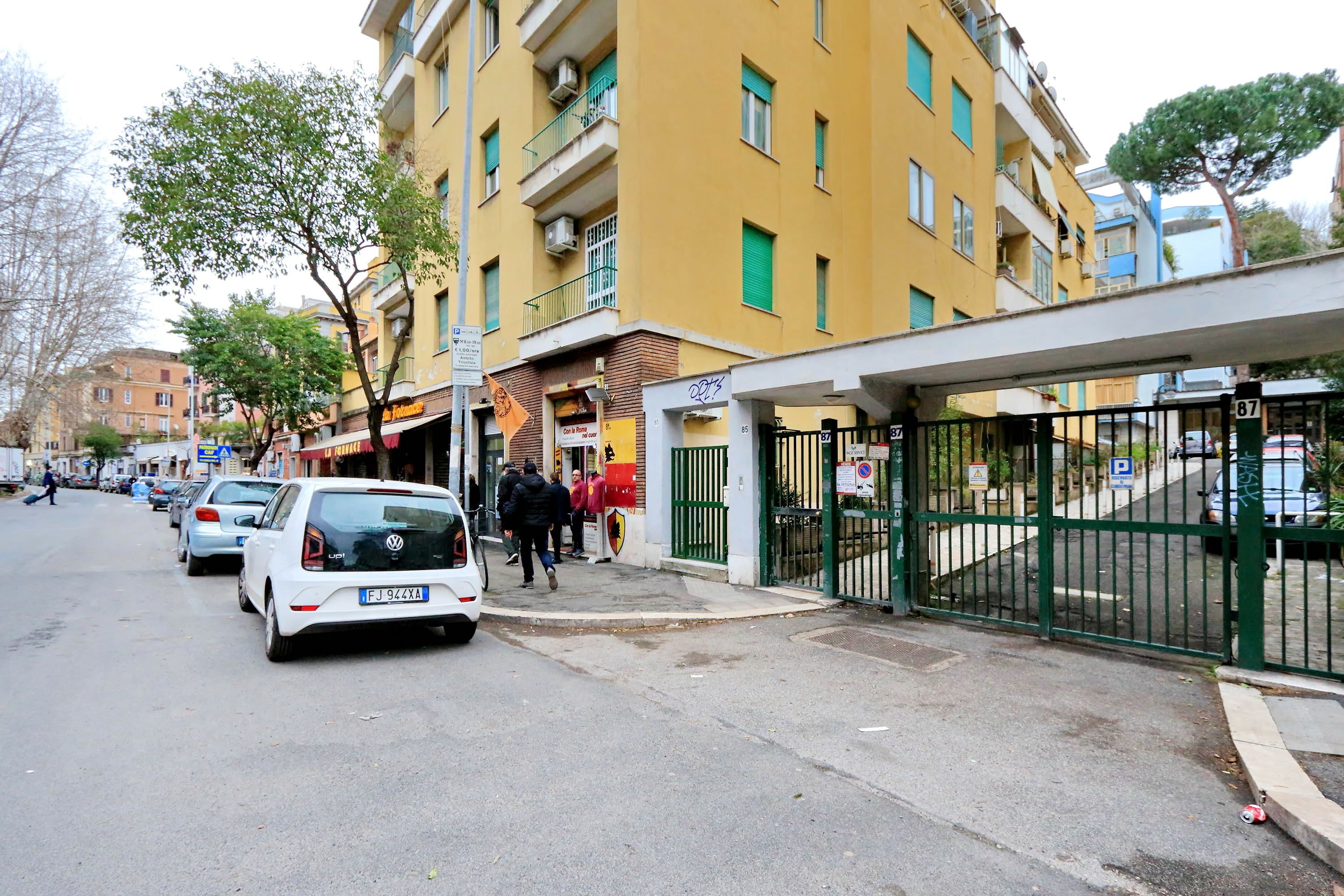 A street with parked cars and a building with a green gate.