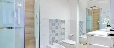 A modern bathroom with a glass shower enclosure, a bidet, a toilet, and a sink with a mirror.