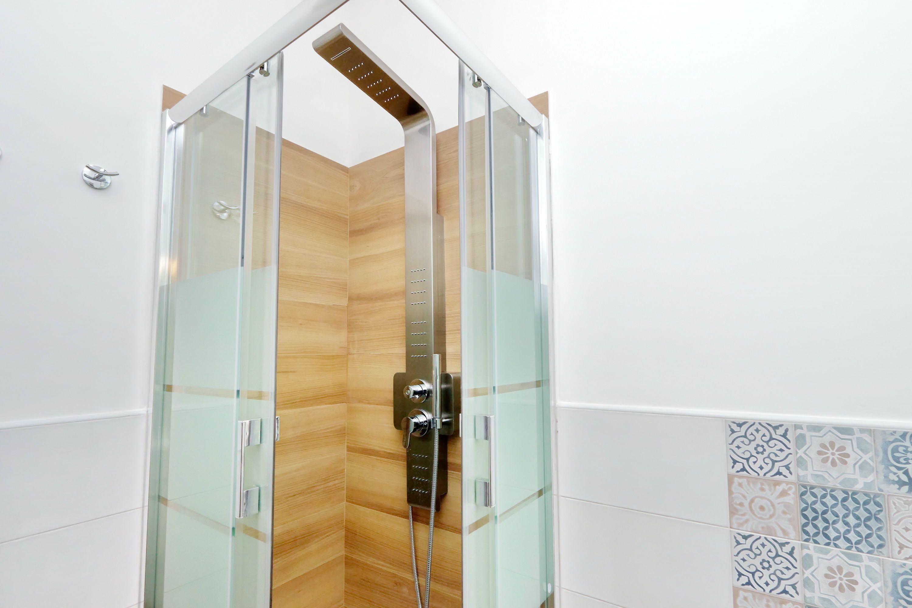 A glass-enclosed shower with a wooden floor and a tiled wall.
