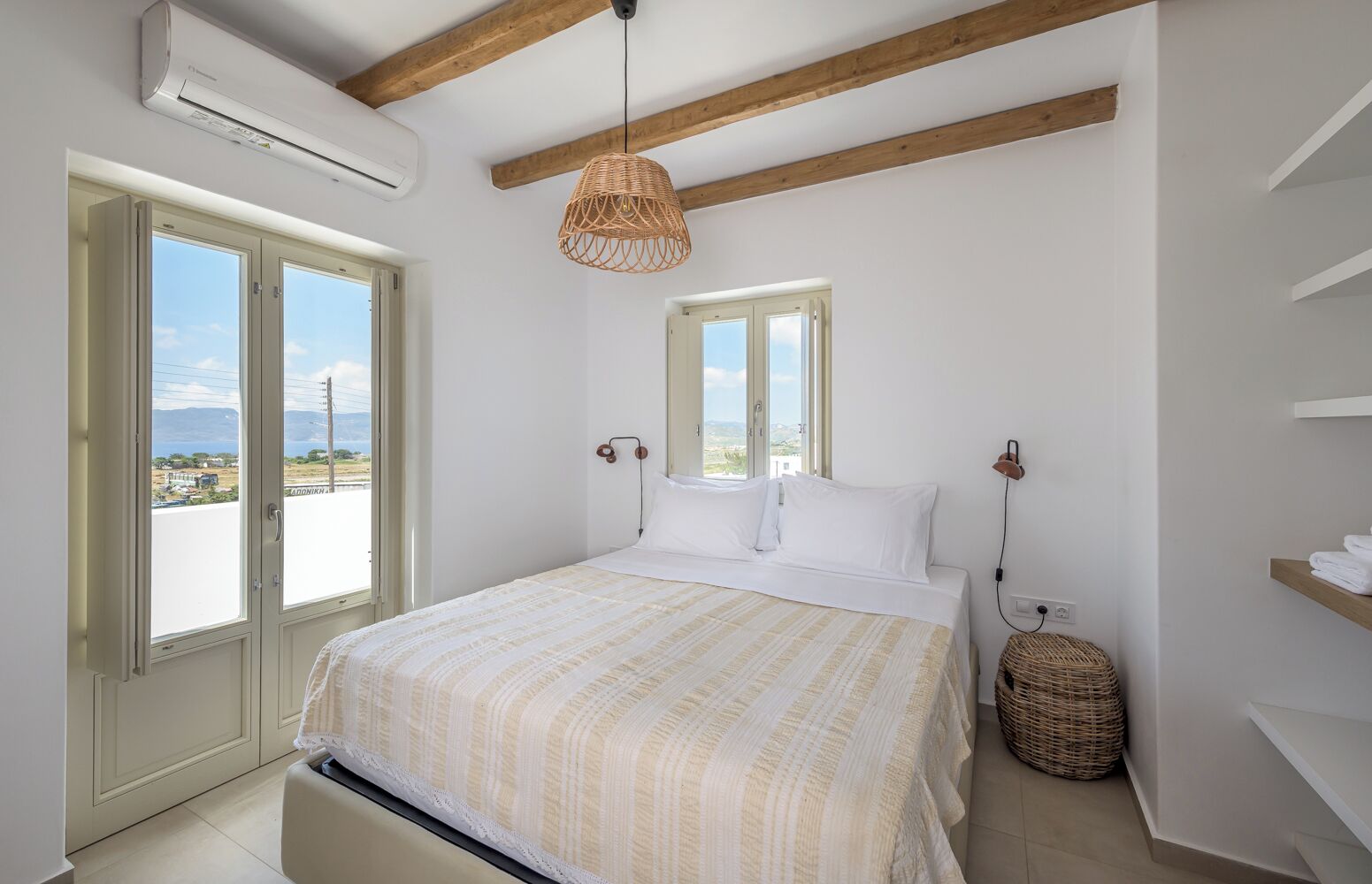 A bedroom with a bed, a hanging light, a wicker basket, and a view of the outside.