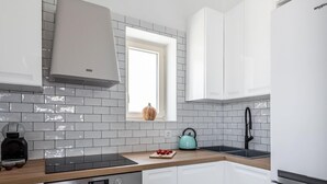 Una cocina moderna con armarios blancos, horno empotrado, refrigerador de acero inoxidable y ventana con vista al exterior.
