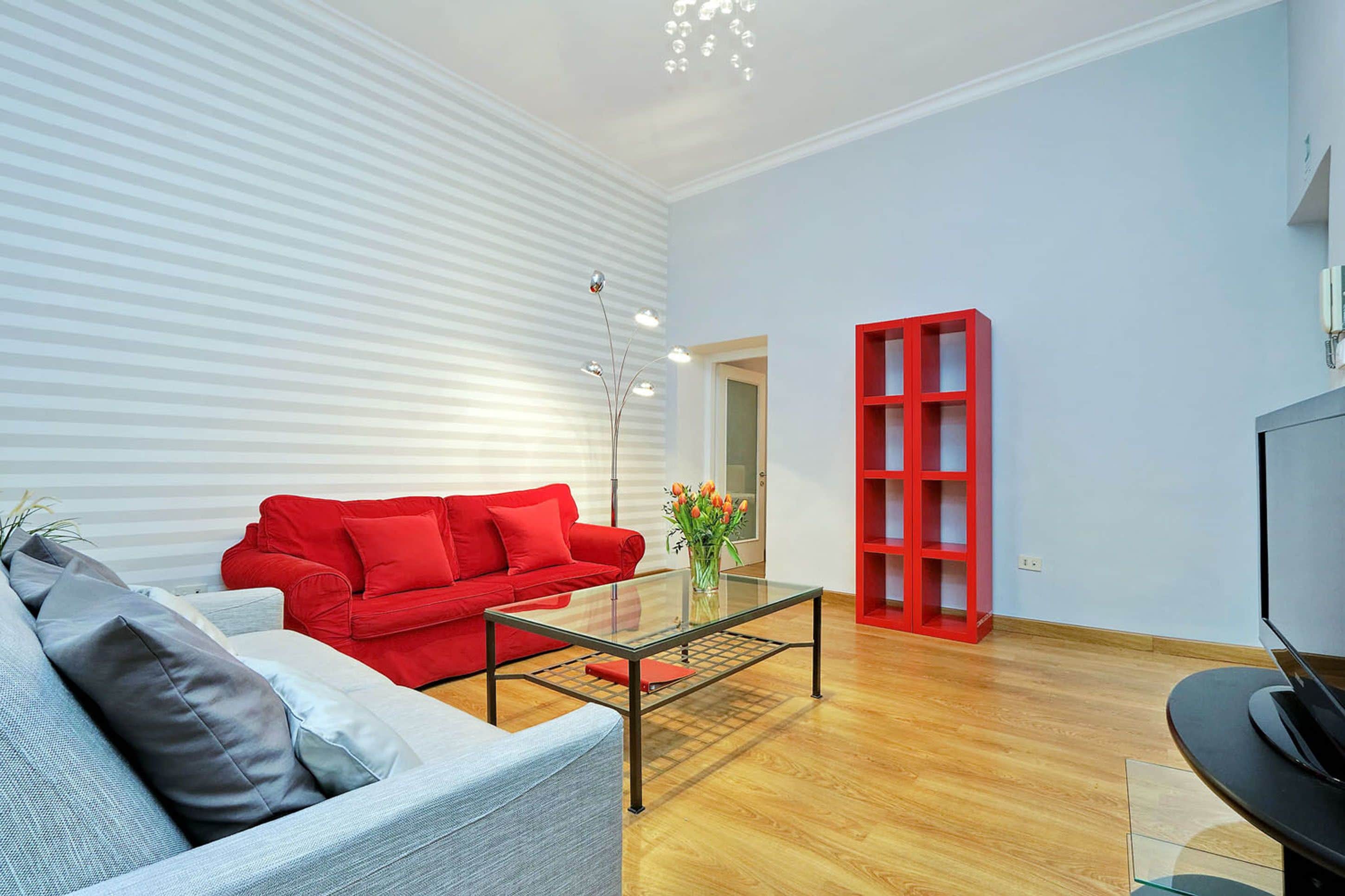A modern living room with a red sofa, a glass coffee table, and a red shelving unit.