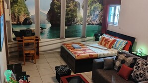 Ein Schlafzimmer mit Bett, Schreibtisch, Stuhl, Sofa und Blick auf eine Küstenlandschaft durch große Fenster.