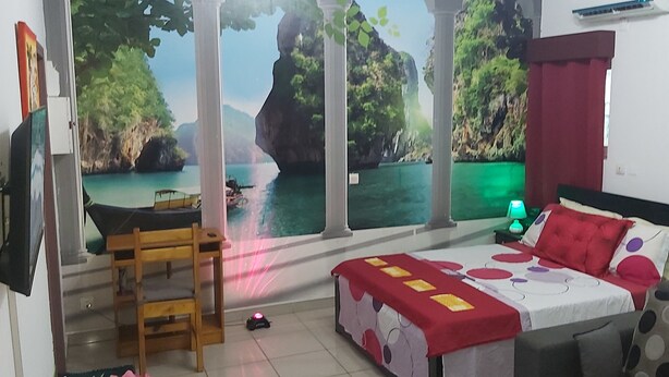 Ein Schlafzimmer mit Bett, Sessel, Schreibtisch und einem großen Fenster mit Blick auf eine Küstenlandschaft.