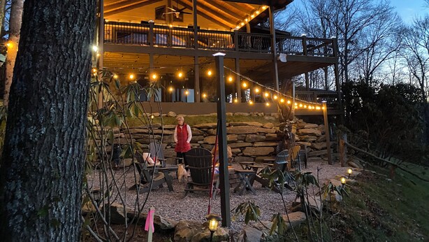 Ein zweistöckiges Blockhaus mit Steinverkleidung, Sitzbereich im Freien und Lichterketten.