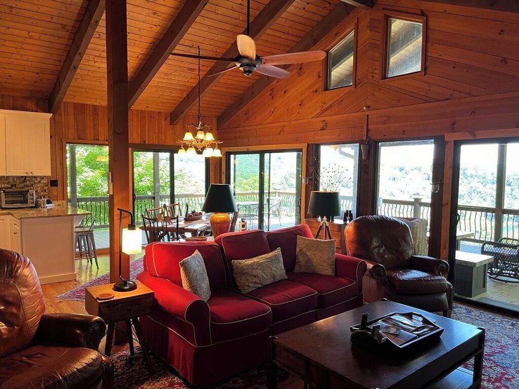 Un salon spacieux avec un canapé rouge, un plafond en bois et de grandes fenêtres donnant sur l’extérieur.