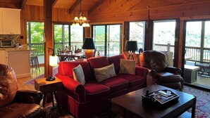 Ein geräumiges Wohnzimmer mit einem roten Sofa, einer Holzbalkendecke und großen Fenstern mit Blick ins Freie.