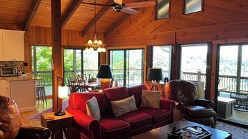 Un salon spacieux avec un canapé rouge, un plafond en bois et de grandes fenêtres donnant sur l’extérieur.