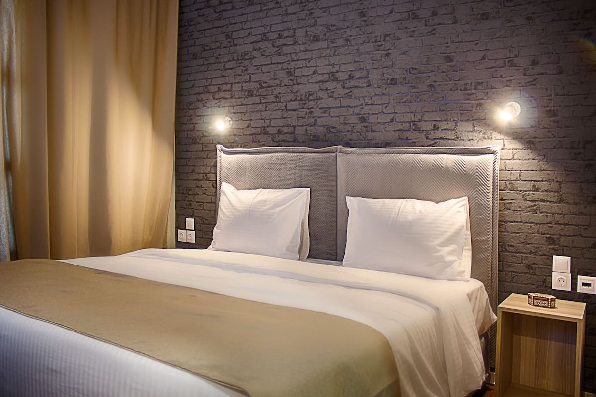 A hotel room with a brick wall, a bed with white bedding, and two wall-mounted lights.