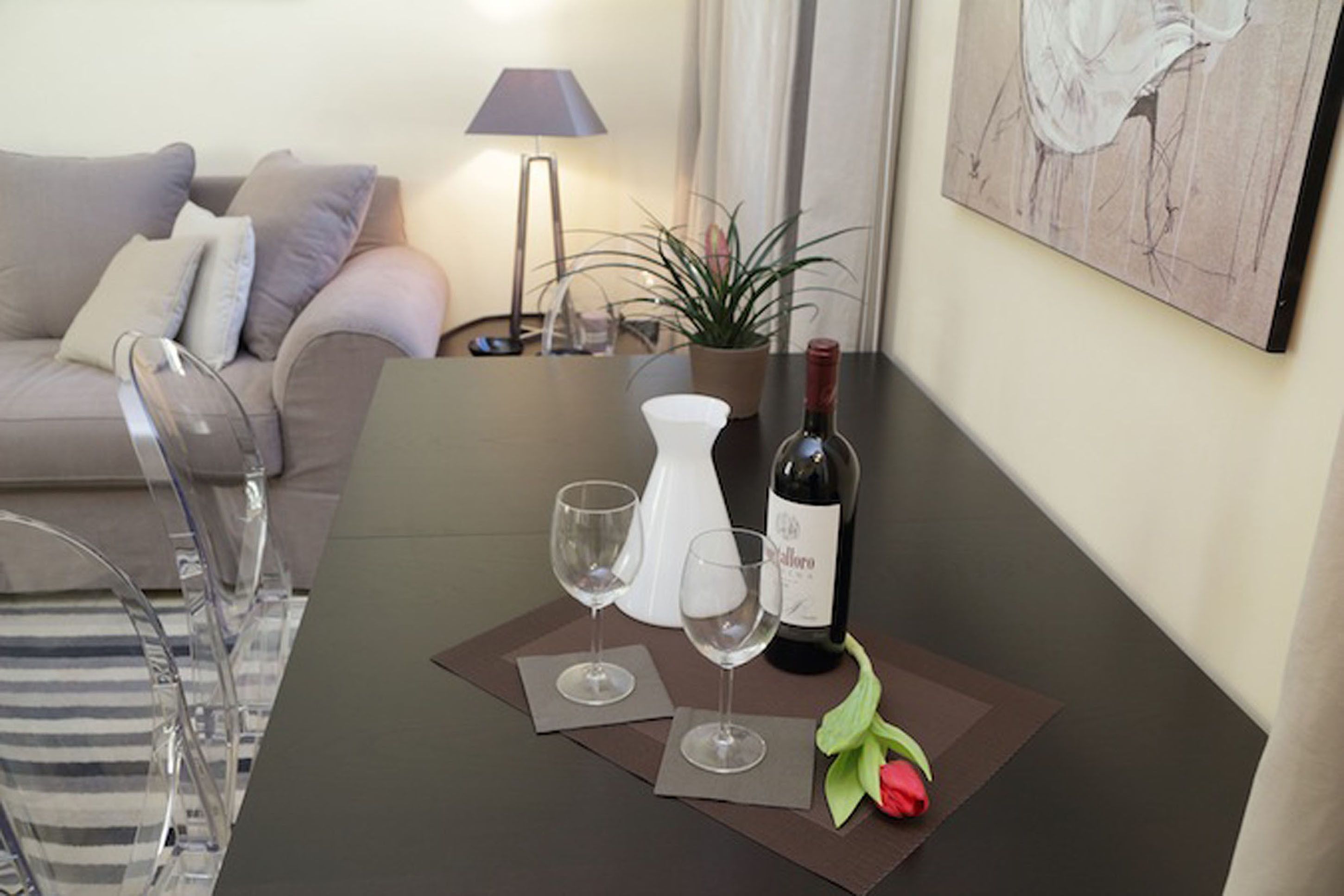 A dining table with two wine glasses, a bottle of wine, a vase, and a potted plant.