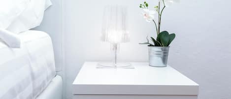 A white bedside table with a lamp and a potted orchid.