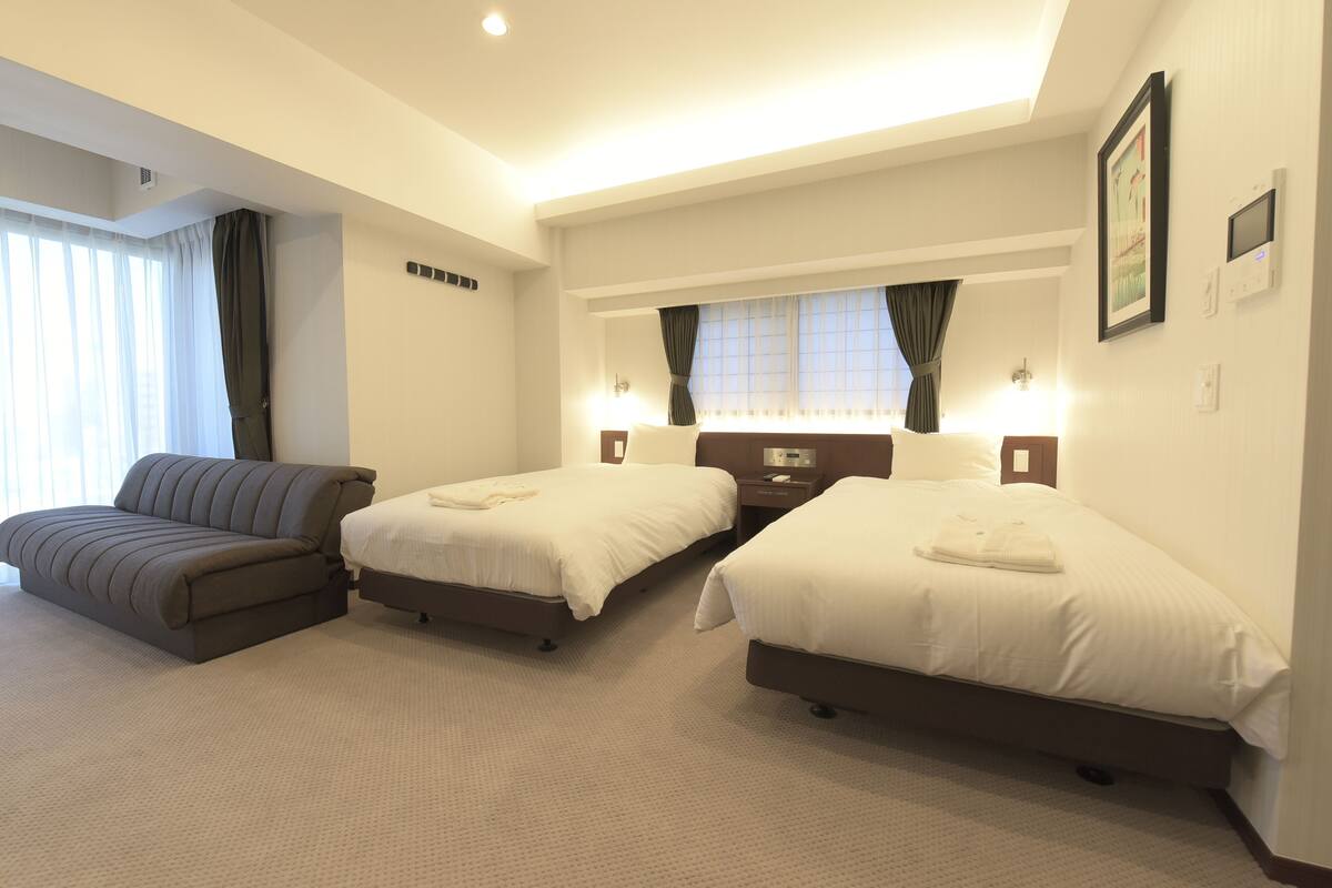 Ein Hotelzimmer mit zwei Betten, einem Sofa, einem Schreibtisch und einem Fenster mit Vorhängen.