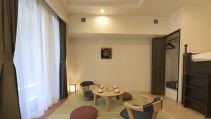 Una habitación con esteras de tatami, una mesa redonda con tazas, sillas, un armario y una cama.