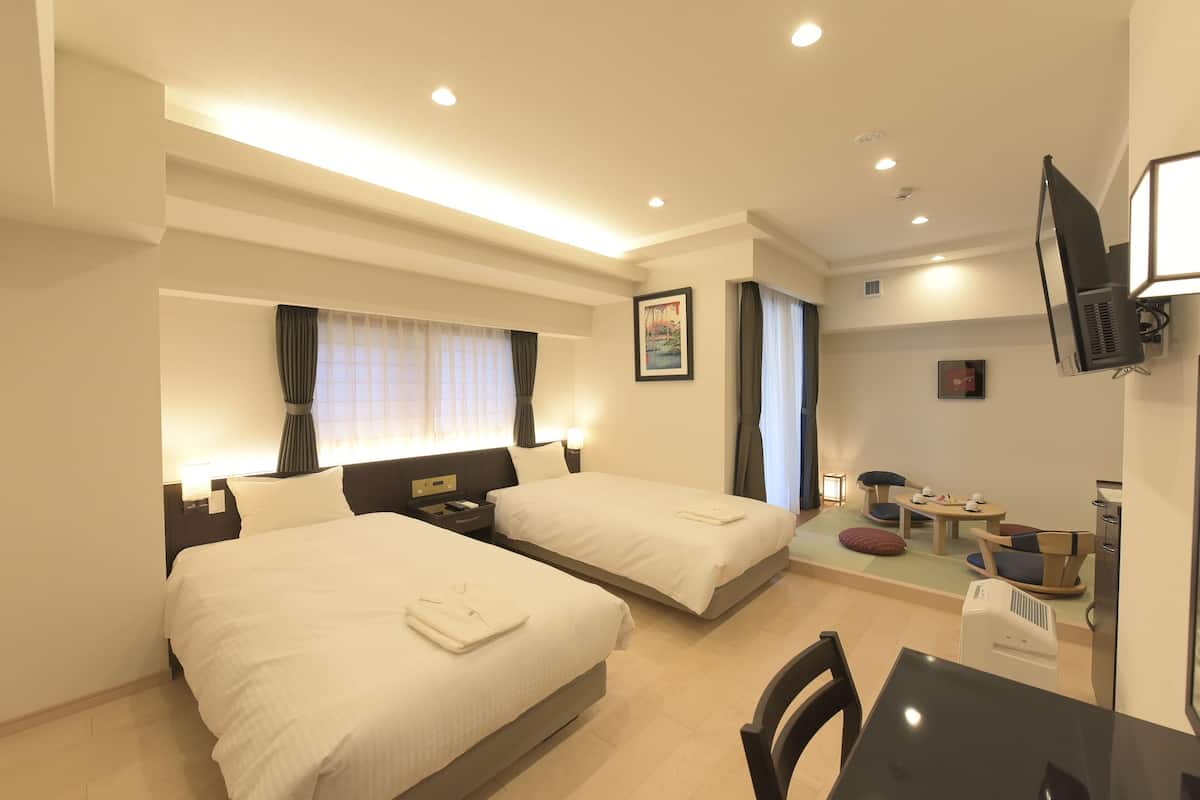 Ein Hotelzimmer mit zwei Betten, einem Schreibtisch, einem Stuhl, einem Fernseher und einer kleinen Sitzecke mit Tisch und Stühlen.