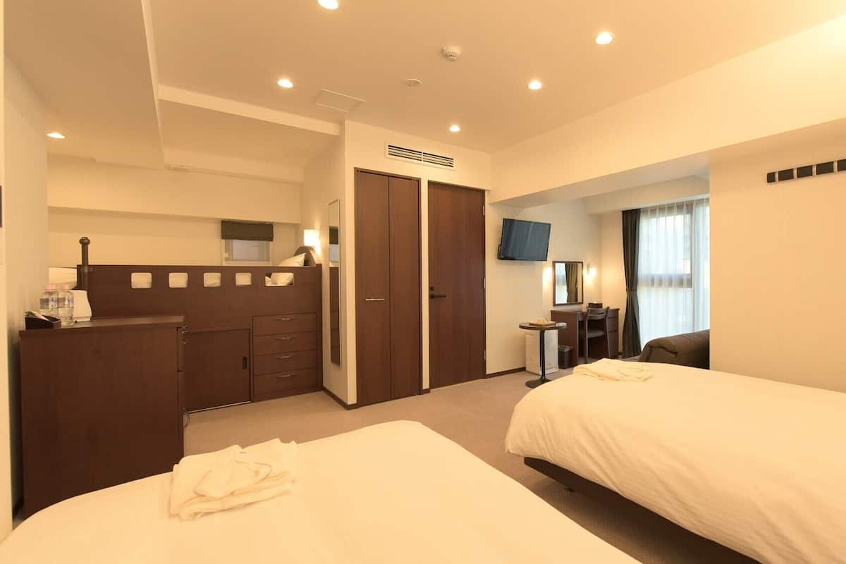Ein Hotelzimmer mit zwei Betten, einem Schreibtisch, einem Fernseher und einem Kleiderschrank.
