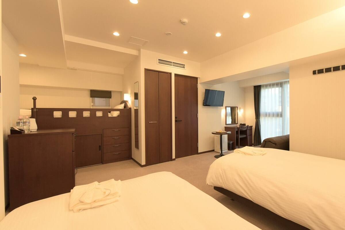 Habitación de hotel con dos camas, un escritorio, un televisor y un armario.