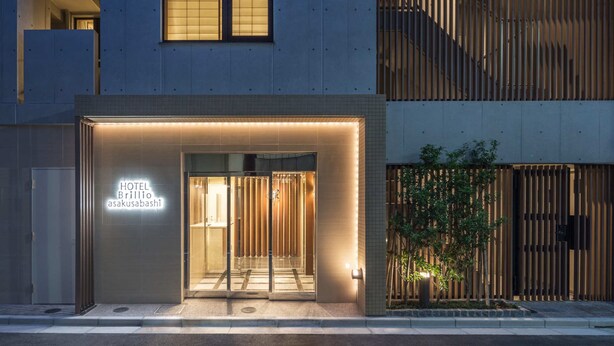Una entrada de hotel moderna con un letrero de neón, puerta de vidrio y diseño de listones de madera verticales a la derecha.