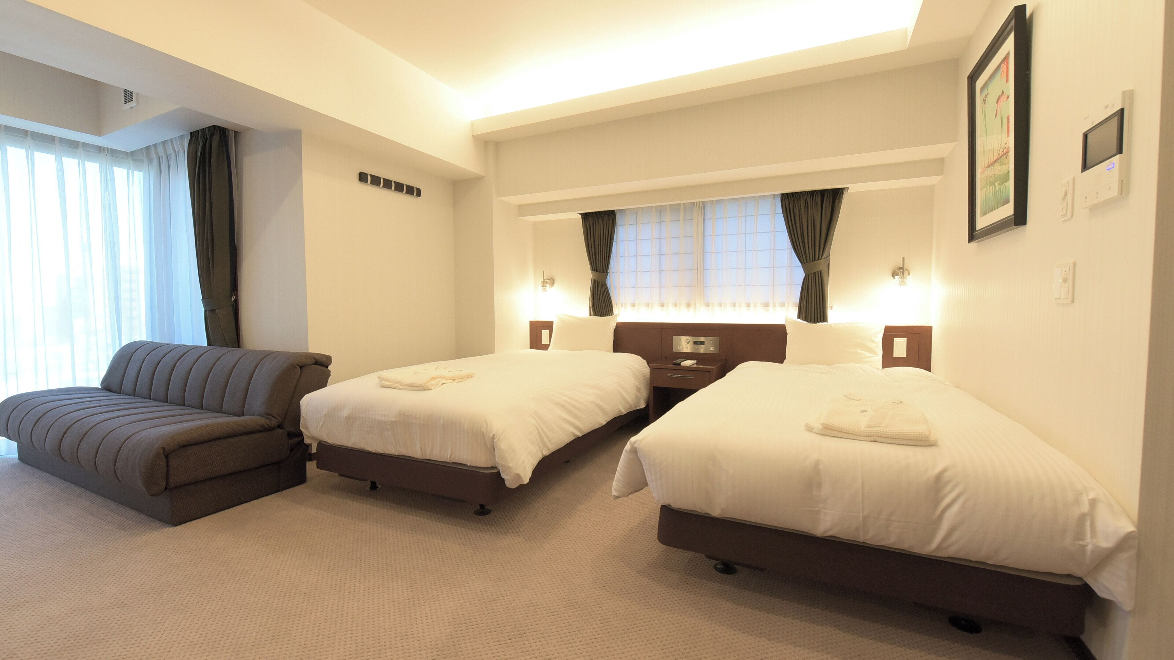 Une chambre d’hôtel avec deux lits, un canapé, une table de chevet avec une lampe et une fenêtre avec des rideaux.