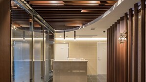 Un moderno vestíbulo de hotel con mostrador de recepción, paredes de vidrio, paneles de madera y suelo de baldosas.