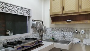 A kitchen with a gas stove, hanging pots, a sink, and a tiled backsplash. - Widi House (Ubud)